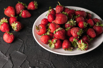 Fresh strawberries in a plate on a black background.