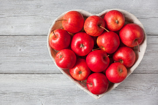 Red apples in a heart-shaped basket on a wooden background