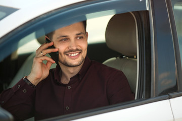 beautiful young guy in a shirt sitting in the car and talking on the phone