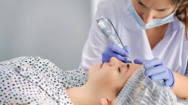 Female beautician in white coat gloves and mask making microblading procedure eyebrows