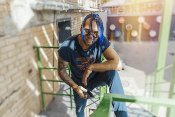 Young man with blue dreadlocks standing on green stairs.