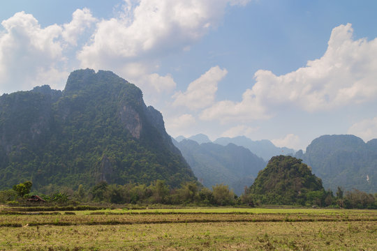 Scenic view of fields, limestone mountains and Pha Poak hill near Vang Vieng, Vientiane Province, Laos, on a sunny day.
