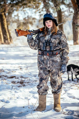 A beautiful hunter in a camouflage suit walks through the woods with weapons, preparing to hunt.