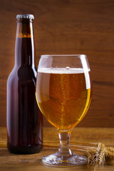 Glass and bottle of beer, ears of barley on wooden background. Ale. vertical