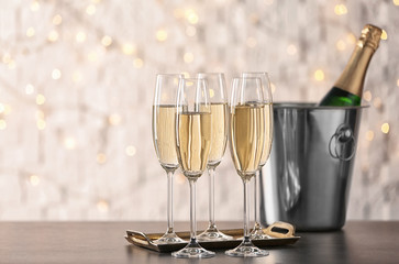 Glasses with champagne and bottle in bucket on table against blurred lights