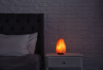 Himalayan salt lamp glowing on bedside table in dark room