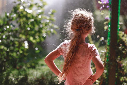 Back view of seven years old blonde girl wearing pyjamas standing outdoor in home garden in the early morning