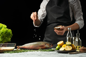 cooking the chief of fresh fish, the chef salt fish on a black background with lemons, limes