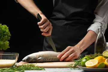Preparation of mackerel by the chef, on a black background with lemons, limes