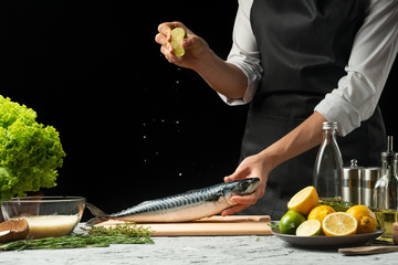Preparation of mackerel by the chef, on a black background with lemons, limes
