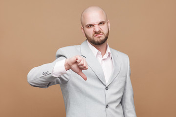 Pointing finger and amazed portrait of handsome middle aged businessman in classic light gray suit standing, looking at camera, wondering and showing brown background. indoor studio shot, isolated.