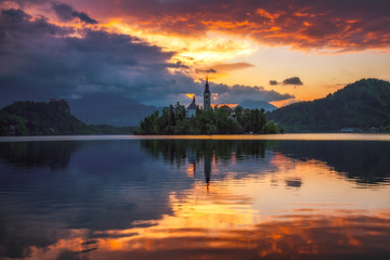 Naklejka premium Dramatic sunrise on lake Bled, sunrise view on Bled lake, island, Pilgrimage Church of the Assumption of Maria and Castle with mountain range (Stol, Vrtaca, Begunjscica). Bled, Slovenia,
