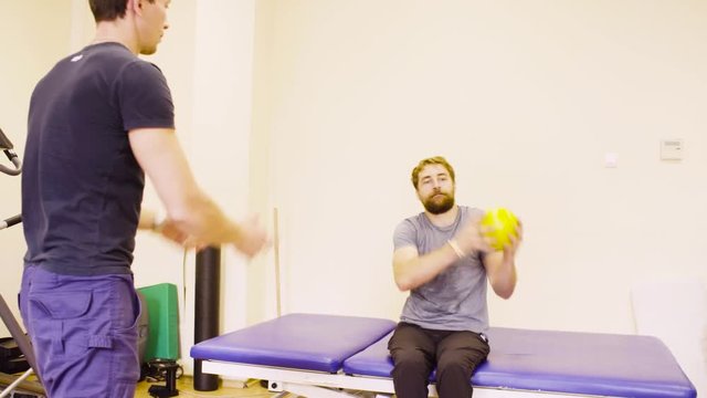 Young disabled man doing hand exercises at the rehabilitation center with a ball. Recovery gymnastics
