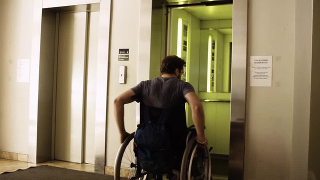 Dolly shot silhouette of young disabled man in a wheelchair outgoing from elevator rehabilitation clinic.
