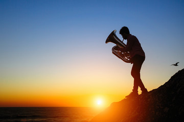 Fototapeta premium Silhouette of a musician play on Tuba on sea shore at sunset .