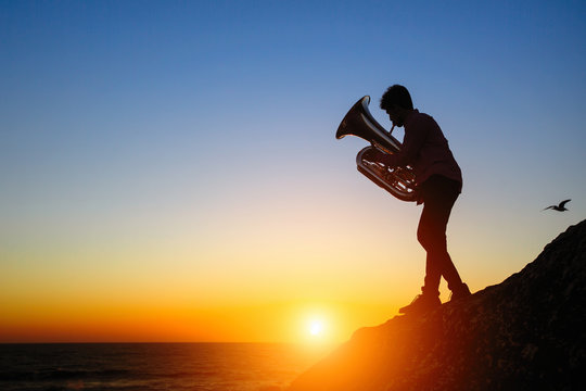 Silhouette of a musician play on Tuba on sea shore at sunset .