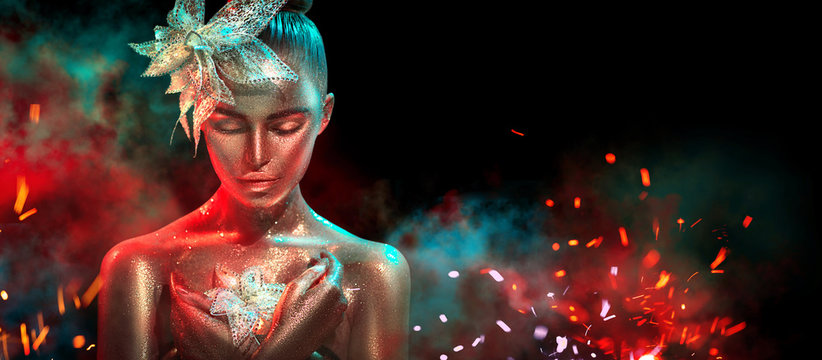 Fashion model woman in colorful bright golden sparkles and neon lights posing with fantasy flower. Portrait of beautiful girl with glowing makeup