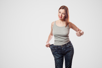 portrait of happy beautiful slim waist of young woman in big jeans and gray top showing successful...