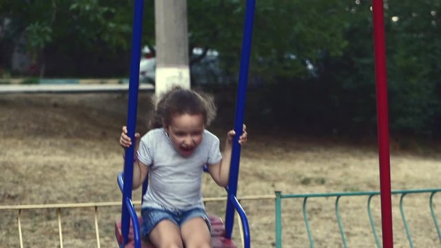 Happy young little girl spinning in a swing and smiling