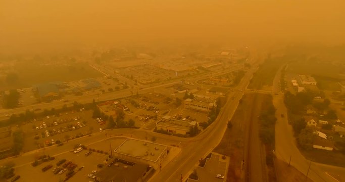 Outward aerial tracking shot of traffic on side roads and highway disappearing in thick bc wildfire smoke - town / city disappearing as well in smoky haze