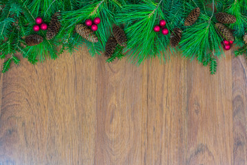 A top border of greenery with pine cones, red berry clusters, and red ribbon