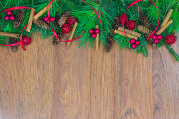 A border of greenery with pine cones, red berry clusters,  red ribbon, ornaments,  and cinnamon sticks