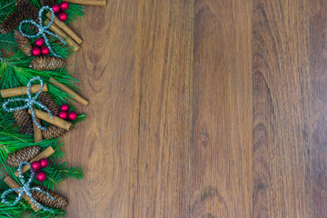 A border of greenery with pine cones, cinnamon sticks, silver bows, and red berries