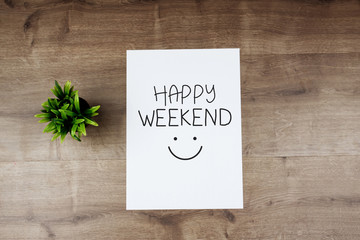 HAPPY WEEKEND text on white template paper and flower on wooden background