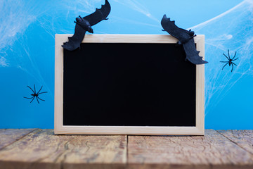 Halloween background concept. Blackboard with decor bat, spider, cobweb on wooden table and blue backdrop