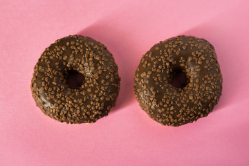 Two glazed chocolate donuts on pink block colour background - minimalism, copy space