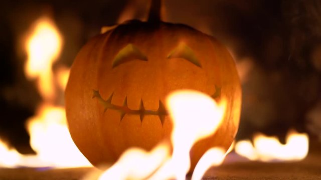 Smiling happy carved halloween pumpkin against of fiery explosion background. Glowing face trick or treat. Orange squash in the center of the fire frame. 4k
