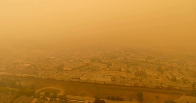 Aerial drone shot of small city covered in smoke from nearby wildfires and forest fires as a BC rail canadian train passes through the small town in BC Canada