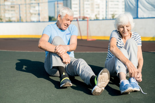 Portrait Of White Haired Senior Couple Tying Sports Shoes Sitting On Running Track Outdoors, Copy Space