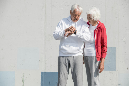 Waist up portrait of modern senior couple setting up smart watch and listening to music while doing morning run in park, copy space