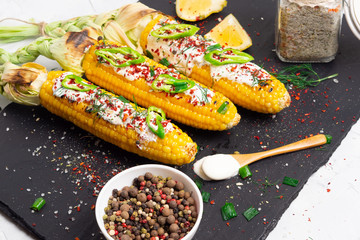Grilled corn with cream sauce, spices, jalapeno on the black stone tile.