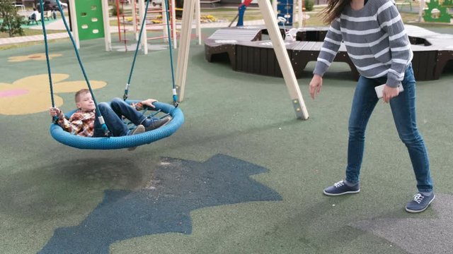 Mom swing son on empty webbed swing.