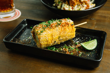 Mexican style grilled corn topping with cheese and chili powder served with sliced lime in black plate. 