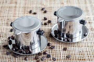 Two coffee makers with scattered whole coffee beans on placemat.