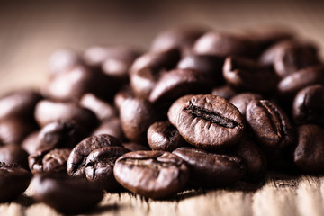 Scattered whole roasted coffee beans on wooden  rustic background.