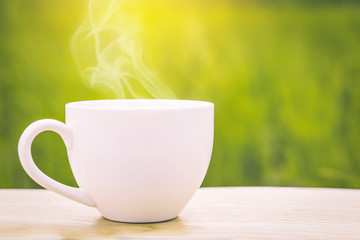 hot coffee cup on wooden table over nature green rice field background with morning sunlight 