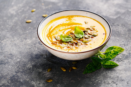 Pumpkin soup in a bowl with basil and pumpkin seeds. Selective focus.