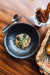 Risotto with mushroom, fresh herb and parmesan cheese in black plate on wooden table.