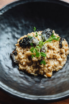 Risotto with mushroom, fresh herb and parmesan cheese in black plate on wooden table.