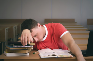 Tired from study a student boy is sitting by the school desk.
