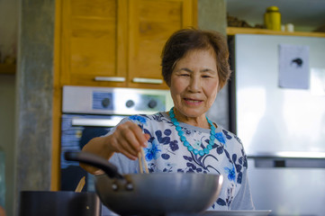 lifestyle portrait of senior happy and sweet Asian Japanese retired, woman cooking at home kitchen...