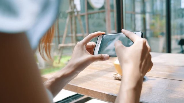 Female blogger photographing coffee cup in cafe with her phone. A young woman taking photo of coffee tea on smartphone, photographing meal with mobile camera.