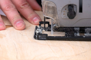 the master holds an electric jigsaw with the other hand supports the workpiece