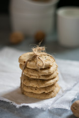 Oatmeal cookies tied with a rope on a white linen napkin, white cup and walnuts in the background