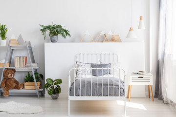 Gray bedding on a single bed with metal frame and a scandinavian style nightstand in a beautiful,...