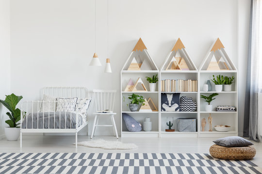Cute pillows and books on wooden shelves units and a chair by a twin bed in an eco bedroom interior for a teenager